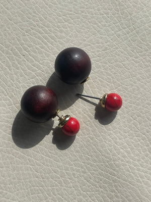 Pair of earrings with red and black spherical stones on a textured beige surface