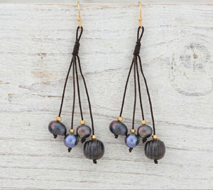 Pair of earrings with pearls and brown strings on a light wooden surface