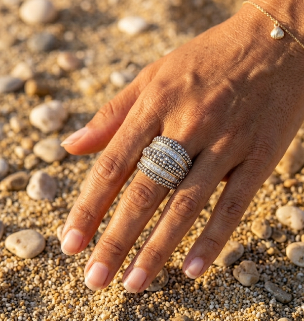 Hand wearing a silver ring on a pebbly surface