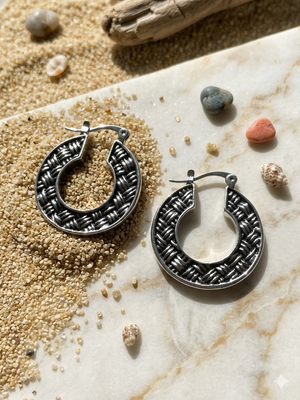 Silver hoop earrings on a textured surface with small stones and pebbles.