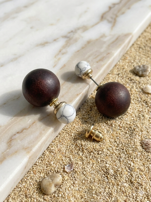 Wooden sphere earrings with marble accents on a marble and sand surface