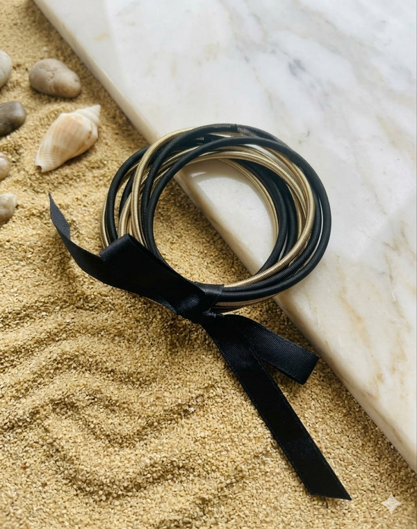 Black and gold hair ties with a black ribbon on sand and marble surface