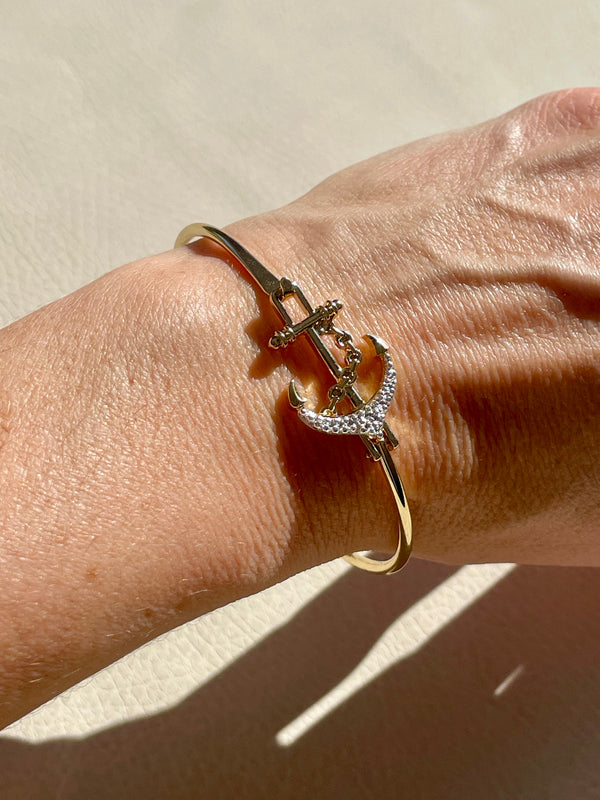 Gold bracelet with anchor design on a wrist against a neutral background