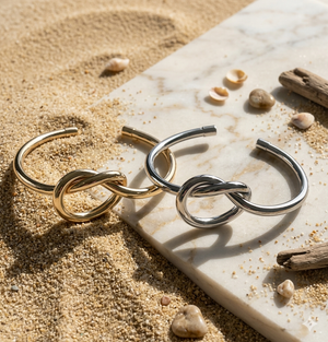 Gold and silver hoop earrings on a marble surface with sand and shells in the background
