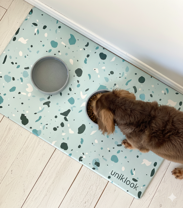 Dog drinking from a bowl on a terrazzo-patterned mat with 'uniklook' branding.