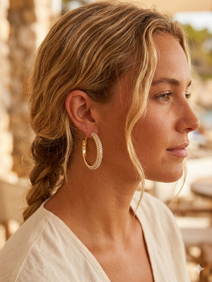 Woman wearing gold hoop earrings with a blurred outdoor background