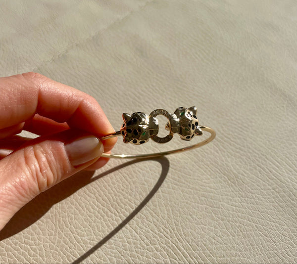 Gold bracelet with cat-shaped charms held by a hand on a beige surface