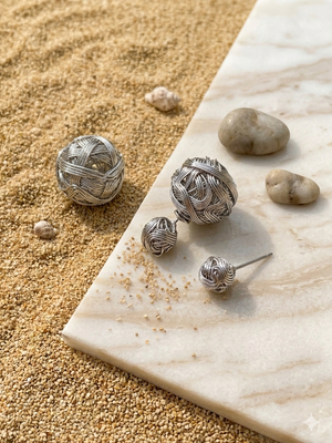Silver spherical earrings on a textured surface with sand and stones