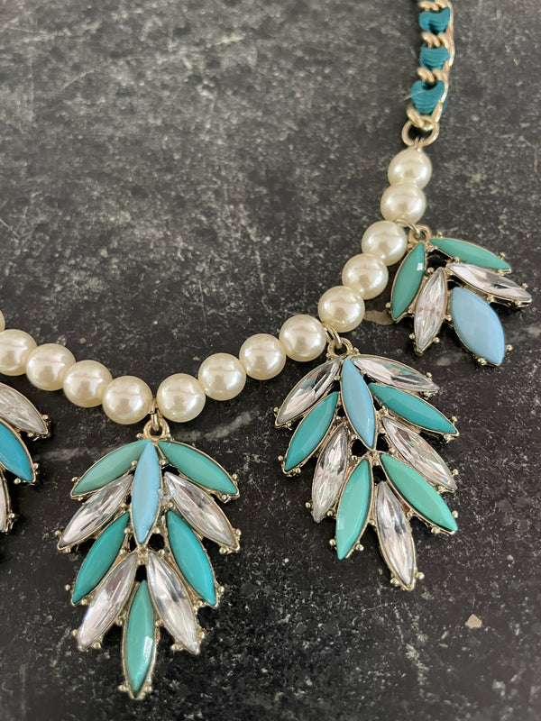 Necklace with pearls, turquoise leaves, and clear stones on a dark background