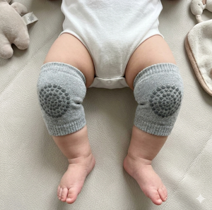 Baby wearing gray knitted knee pads on a light-colored surface