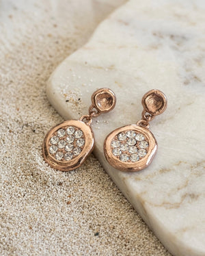 Rose gold earrings with gemstones on a stone surface
