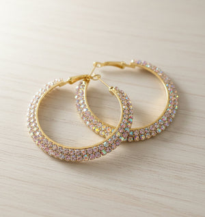 Gold hoop earrings with gemstones on a light wooden surface