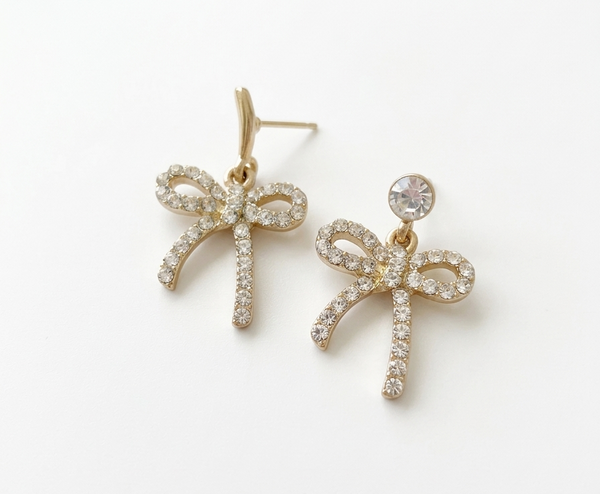 Gold bow-shaped earrings with clear stones on a white background