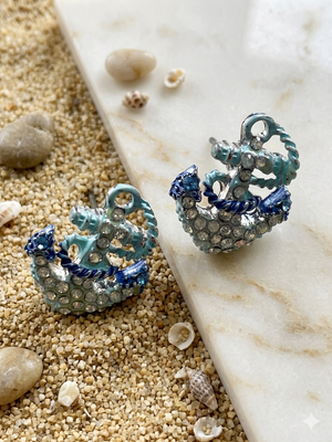 Pair of decorative earrings on a sandy surface with shells.
