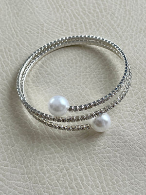 Two pearl-studded silver bracelets on a light gray textured surface