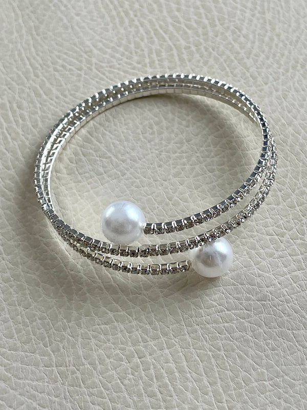 Two pearl-studded silver bracelets on a light gray textured surface
