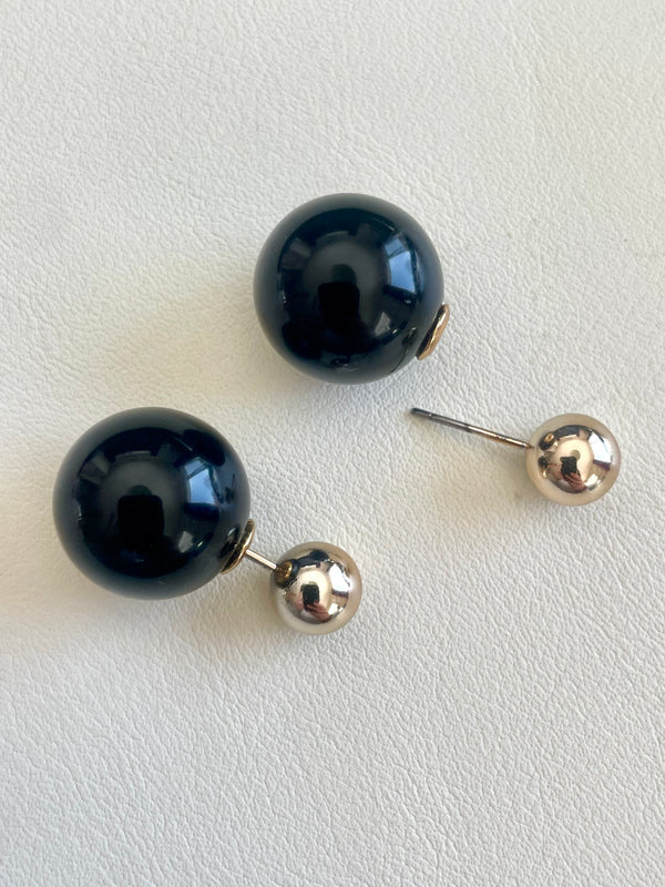 Black spherical earrings with gold posts on a light gray background
