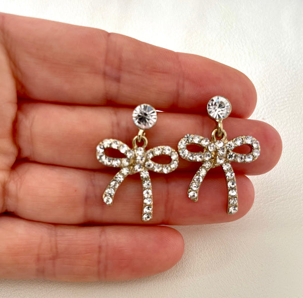 Bow-shaped earrings with rhinestones held between fingers on a light background