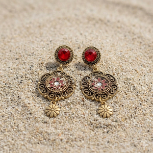 Ornate earrings with red gemstones on a sandy surface