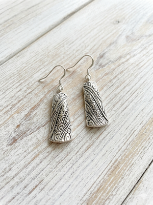 Silver earrings with intricate designs on a wooden surface