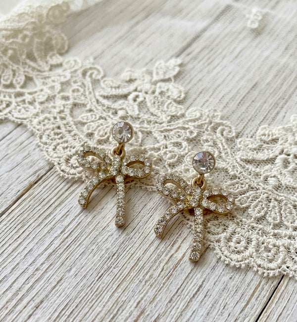 Gold bow-shaped earrings with rhinestones on a lace fabric background