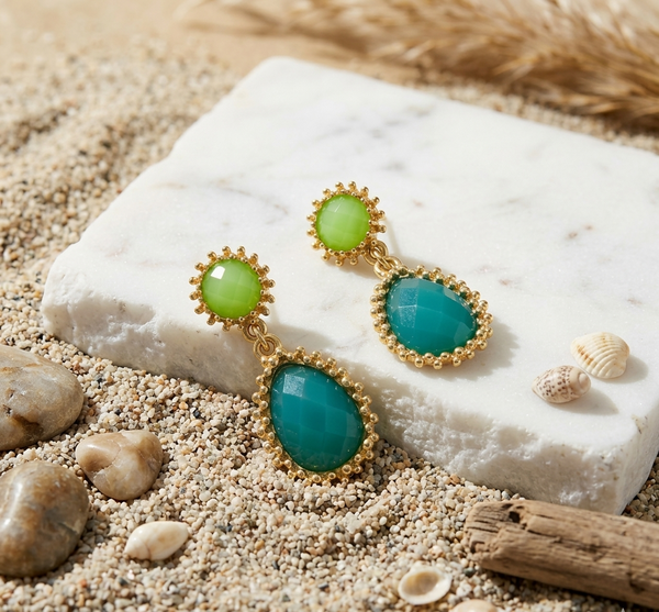 Pair of earrings with green gemstones on a white stone with beach elements.