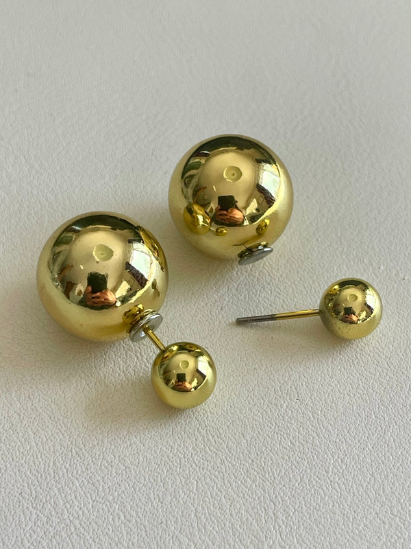 Gold spherical earrings on a light gray background