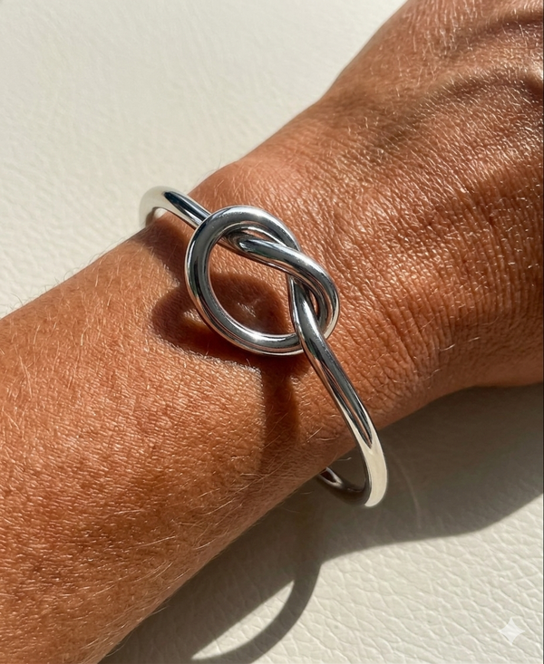 Silver knot bracelet on a wrist against a neutral background