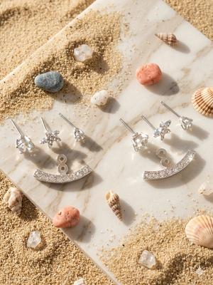 Silver earrings on a marble surface with seashells and sand around