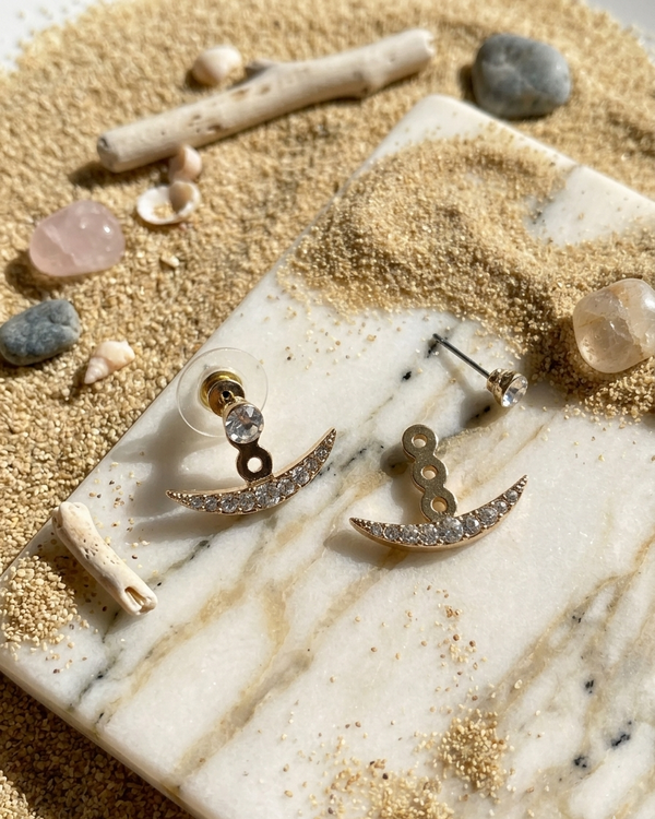 Gold earrings on a marble surface with sand and stones in the background