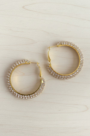 Gold hoop earrings with clear gemstones on a dark textured surface