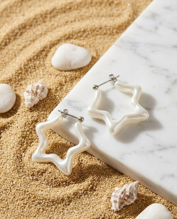 Star-shaped earrings on a marble surface with sand and shells around