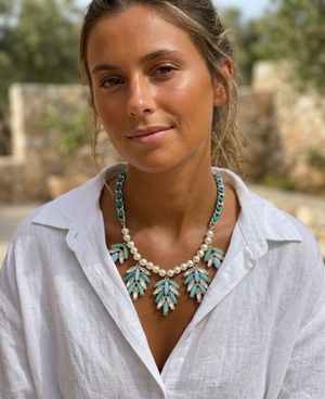 Woman wearing a white shirt and a decorative necklace with green leaves and pearls outdoors.