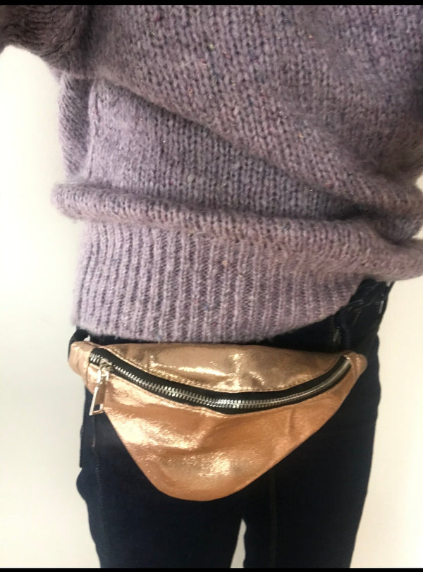 Person wearing a metallic fanny pack on a plain background