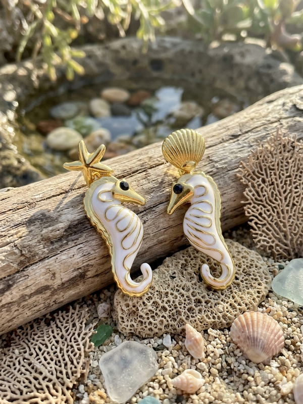 Gold and white seahorse earrings on a natural background with coral and shells.