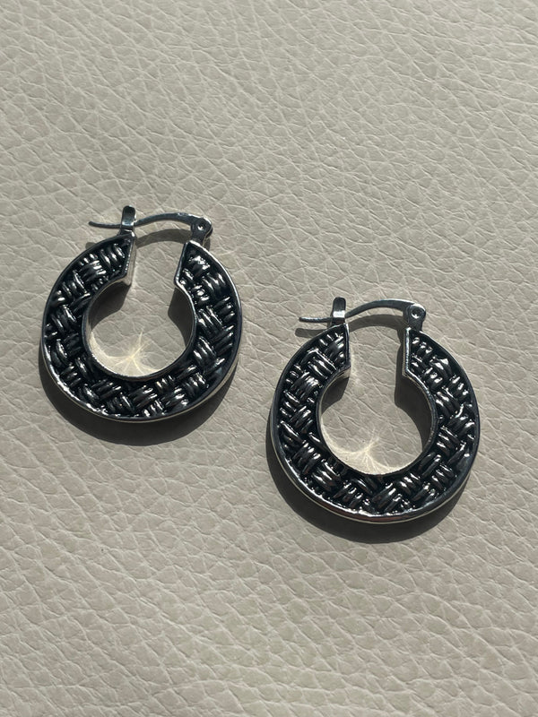 Pair of black hoop earrings on a beige textured surface