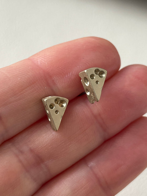 Two small metallic triangle-shaped objects held between fingers against a neutral background