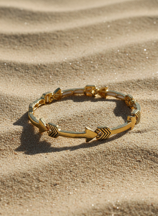 Gold bracelet with arrow designs on a sandy surface