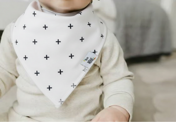 Child wearing a white bib with black cross patterns and a visible brand tag.