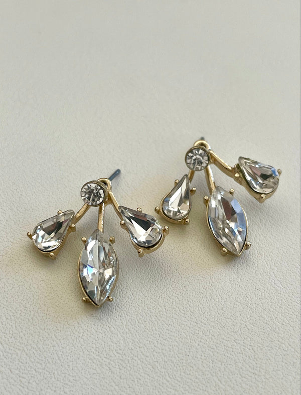 Gold earrings with clear gemstones on a light gray background