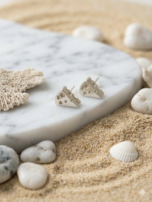 Silver heart-shaped earrings on a marble stone with seashells and coral.