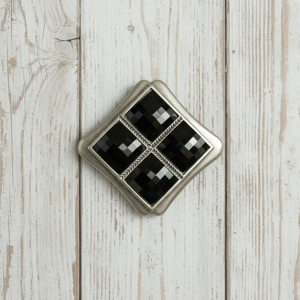 A vintage-style diamond-shaped brooch featuring four inset black faceted gemstones divided by a silver cross, set within a textured silver border on a white background.