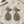 Load image into Gallery viewer, Pair of sparkling earrings on a sandy surface with driftwood and shells.
