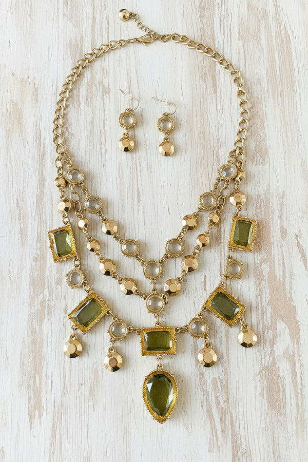 Necklace and earrings set with green and clear stones on a dark surface