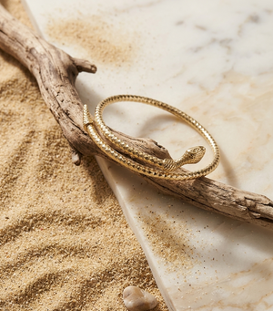 Gold bracelet on a branch with sand and stone in the background