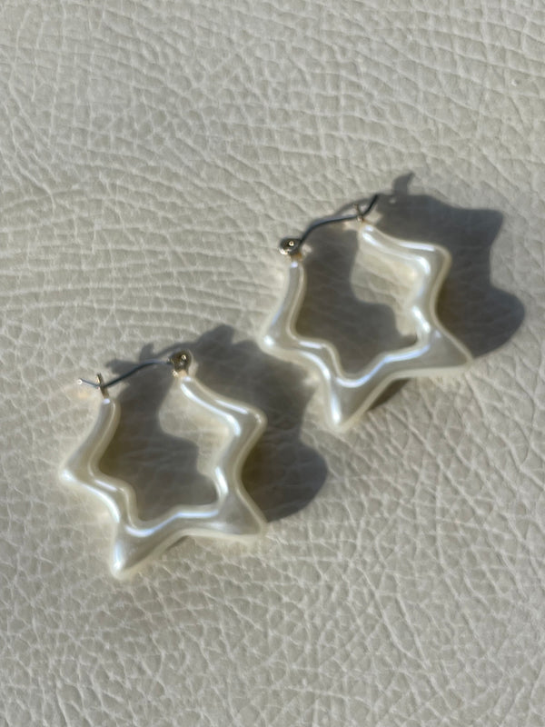 Star-shaped silver earrings on a textured beige surface