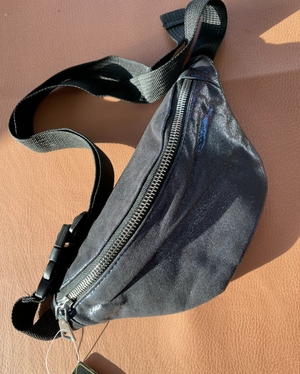 Black waist bag on a beige surface with a visible brand tag.