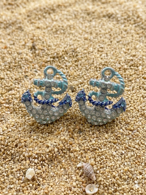 Anchor-shaped earrings with blue accents on a sandy surface