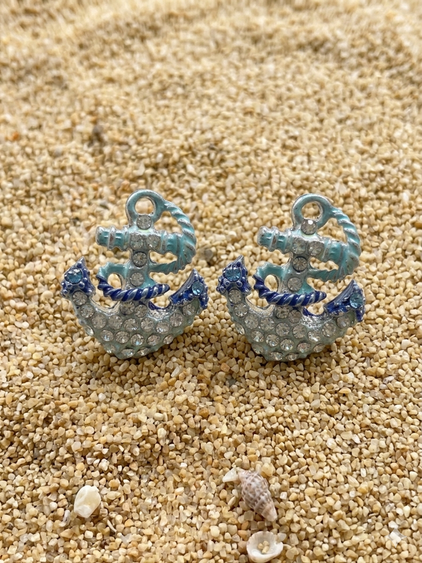 Anchor-shaped earrings with blue accents on a sandy surface
