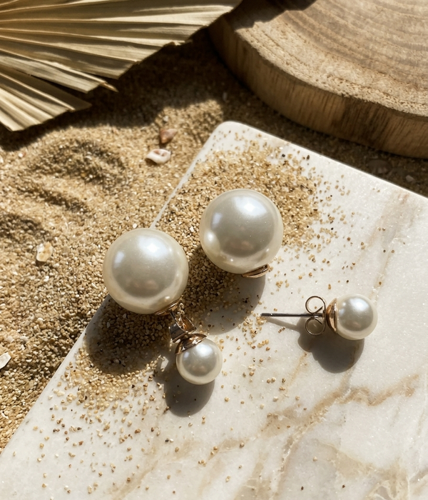 Pearl earrings on a textured surface with sand and leaf